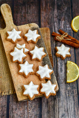 Traditional German bread   Christmass stollen  cake ,gingerbread star shaped   cookies and cinnamon sticks    on   wooden background with lights . Christmas  card background  . Holiday wallpaper