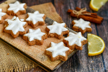 Traditional German bread   Christmass stollen  cake ,gingerbread star shaped   cookies and cinnamon sticks    on   wooden background with lights . Christmas  card background  . Holiday wallpaper