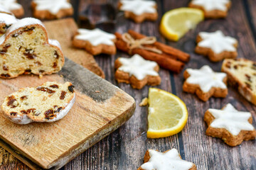 Traditional German bread   Christmass stollen  cake ,gingerbread star shaped   cookies and cinnamon sticks    on   wooden background with lights . Christmas  card background  . Holiday wallpaper