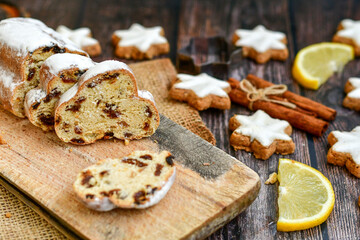 Traditional German bread   Christmass stollen  cake ,gingerbread star shaped   cookies and cinnamon sticks    on   wooden background with lights . Christmas  card background  . Holiday wallpaper