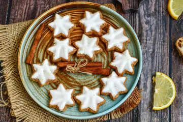 Gingerbread star shaped   cookies and cinnamon sticks    on   wooden background with lights . Christmas  card background  . Holiday wallpaper