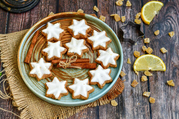 Traditional German bread   Christmass stollen  cake ,gingerbread star shaped   cookies and cinnamon sticks    on   wooden background with lights . Christmas  card background  . Holiday wallpaper