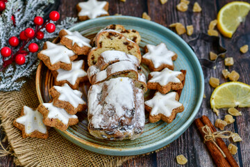 Traditional German bread   Christmass stollen  cake ,gingerbread star shaped   cookies and cinnamon sticks    on   wooden background with lights . Christmas  card background  . Holiday wallpaper