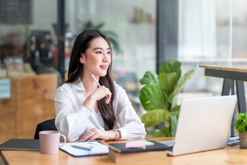 Portrait of smiling beautiful Asian businesswoman enjoy the idea sitting at office.