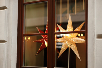Stylish christmas stars in window, decorations of building or shops in european city street. Modern...