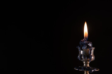 Burning black candle. Stands in an old brass metal candlestick. Black background. Vintage style concept, dramatic and mystic. Copy space