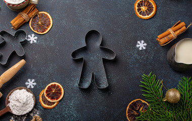 Christmas and New Year baking composition with kitchen tools, flour, milk, balls, fir tree and gingerbread man cutter in center on dark blue stone concrete background table top view