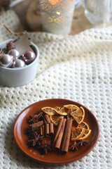 Plate with cinnamon, anise and dry oranges, cozy blanket, various Christmas deocrations and lit candles. Hygge at home. Selective focus.