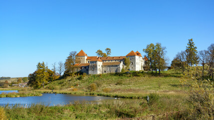 Autumn landscape with a view of the Svirzh castle and a pond, Ukraine. Sunny leaf fall day. An ancient fortification sits amid ponds and moats.