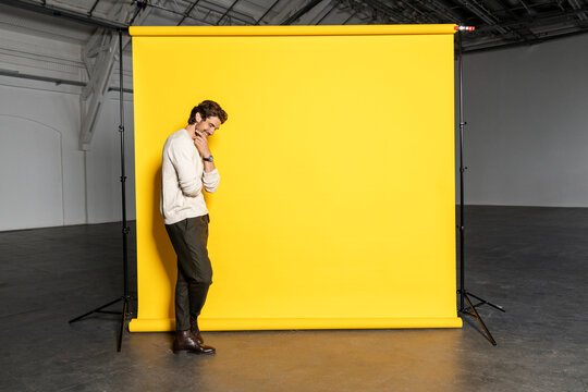 Businessman with hand on chin by yellow backdrop at industrial hall