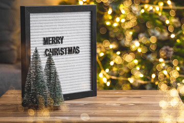 A sign with the inscription Merry Christmas on a wooden table top. Beautiful bokeh on a golden background. New Year's background 2022 for the demonstration or installation of products and goods.