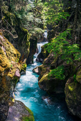 Clear turqoise water cascades over red rock waterfalls on Avalanche Creek in Glacier National Park...
