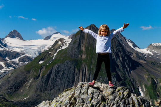 Girl with arms outstretched standing on rock, Nufenen Pass, Switzerland