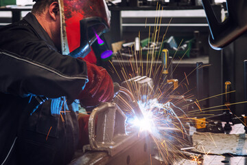 A heavy industrial worker in a factory works with metal on angle grinders while hot sparks are produced as a result.