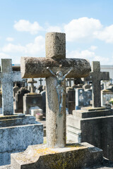 Stone cross with Jesus and graves with more crosses in the cemetery blurred behind