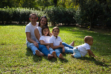 Fototapeta premium Portrait of happy parents with their three children lying in the park. The eldest daughter is a transgender girl. Concept of family happy united family with children.