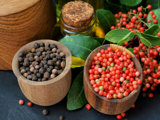 Black peppercorns, pink peppercorns in a composition with herbs and olive oil. Close-up