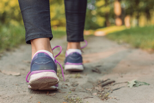 Crop person legs in sneakers on ground lawn in forest