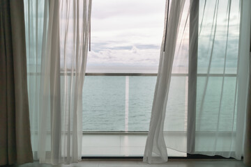 Almost evening time of ocean view from hotel balcony with curtains.