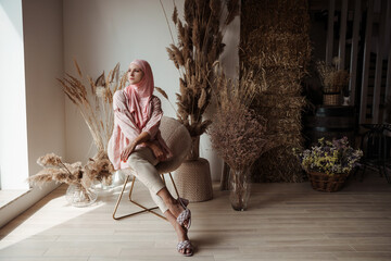 Beautiful muslim arabian woman wearing pink hijab sitting on floor and smiling - obrazy, fototapety, plakaty