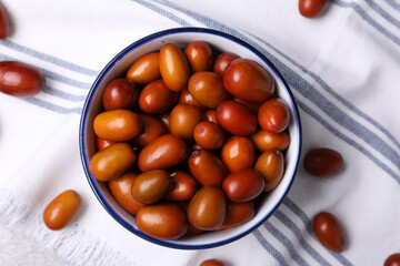 Fresh Ziziphus jujuba fruits in bowl on napkin, flat lay