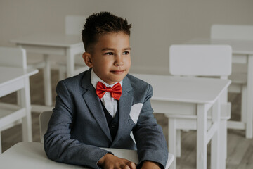Schoolboy wearing red bow tie with suit sitting in classroom