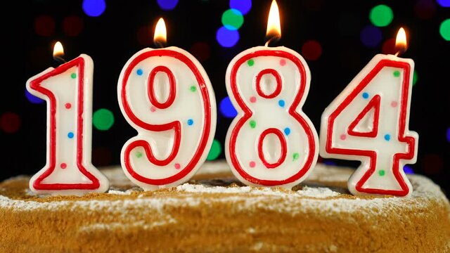 Birthday cake with white burning candles in the form of number 1984