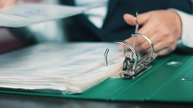 Female accountant's hands put the accounting documents in a folder with an iron clip. The woman carefully stacks the documents and uses a special clamping mechanism. Accounting statements.