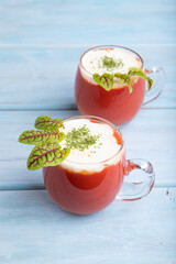 Tomato juice with sorrel and sour cream in glass on blue wooden background. Side view, close up.