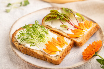 White bread sandwiches with cream cheese, calendula petals and microgreen on gray. side view, selective focus.