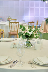 Beautiful floral arrangement of rose flowers and greenery on wedding table in restaurant, copy space. Luxury wedding decorations. Table setting
