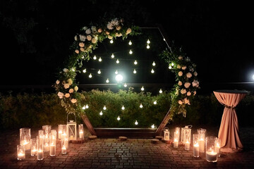 Night wedding ceremony with circle arch, flowers, bulb lights and candles on the backyard outdoors, copy space. Wedding decor