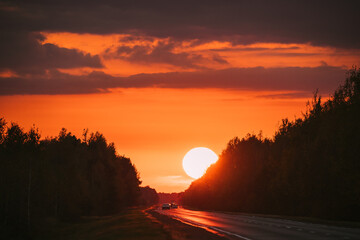 Cars In Motion On Road, Freeway. Asphalt Motorway Highway Against Background Of Big Sunset Sun. Travel Trip Concept. Sunshine Above Road