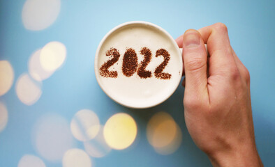 Hand holding cup of coffee with 2022 numbers. New Year greeting. Fresh start concept