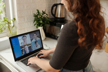 Young businesswoman standing at kitchen counter and attending online conference with colleague