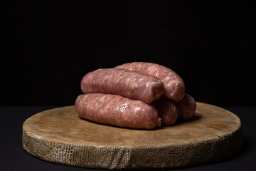 Raw meat sausages on a wooden board on a black background. Homemade sausages in a natural casing. Meat products