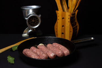 Raw meat sausages in a frying pan on a black background. Homemade sausages in a natural casing. Meat products. Home cooking