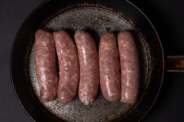 Raw meat sausages in a frying pan on a black background. Homemade sausages in a natural casing. Meat products. Home cooking