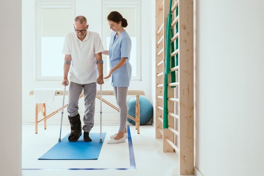 Injured patient in a leg brace exercising on a blue mat in a physiotherapy office