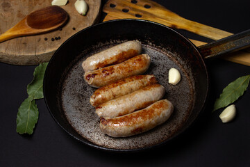 Fried meat sausages in a skillet on a black background. Homemade sausages in a natural casing. Meat products. Home cooking