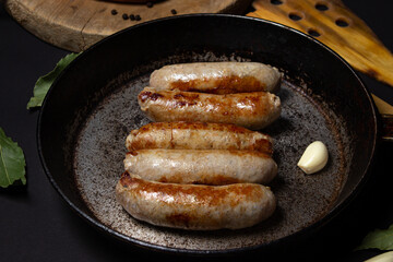 Fried meat sausages in a skillet on a black background. Homemade sausages in a natural casing. Meat products. Home cooking