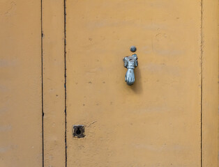 Rustic orange door, with metal handle in the shape of a hand.