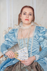 Beautiful young woman in medieval style blue dress with fan