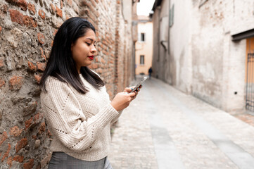 Side view young latin woman using smartphone in an alley