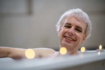 Mensch nimmt lächelnd ein Bad mit Kerzen auf dem Wannenrand