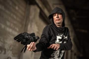 Stehender Mensch mit Rabe in der Hand schaut neugierig auf den Vogel