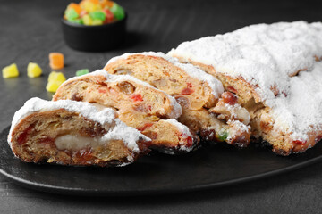 Traditional Christmas Stollen with icing sugar on black table, closeup