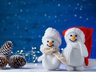 Nice couple. Knitted snowman toys on a blue wooden background . Garland, Christmas cones and...