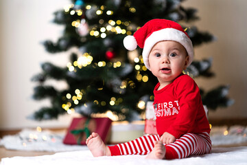 adorable little baby boy in a red christmas outfit sitting on a soft fake fur in front of a...