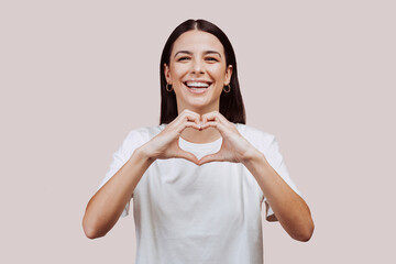 Close up portrait of beautiful caucasian young woman doing love hearth sign with hands at the...